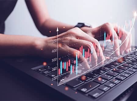 Hands typing on a laptop keyboard with floating financial metrics graphics